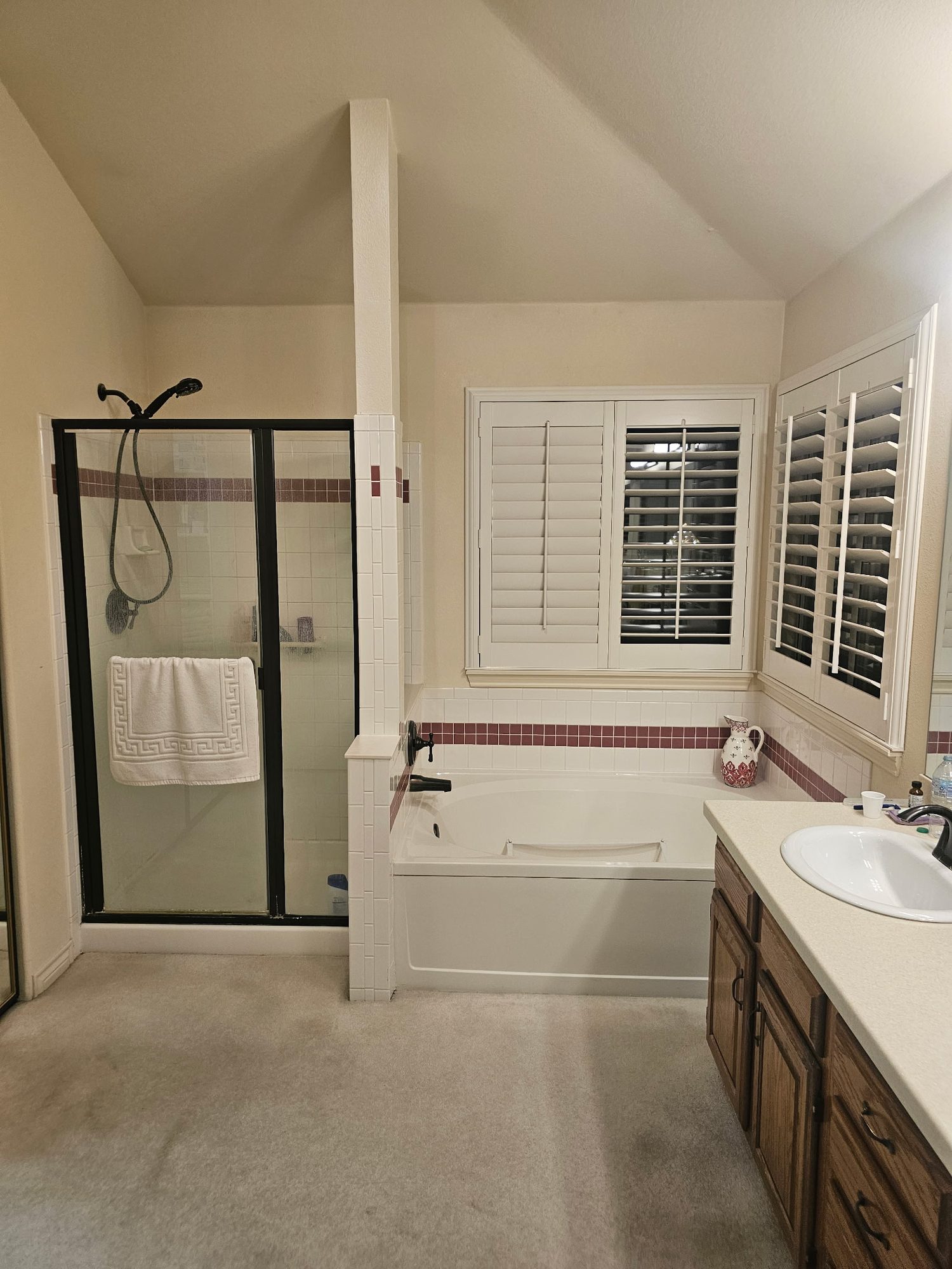 Primary bath before: carpet, dated tile band, framed shower and oak vanity